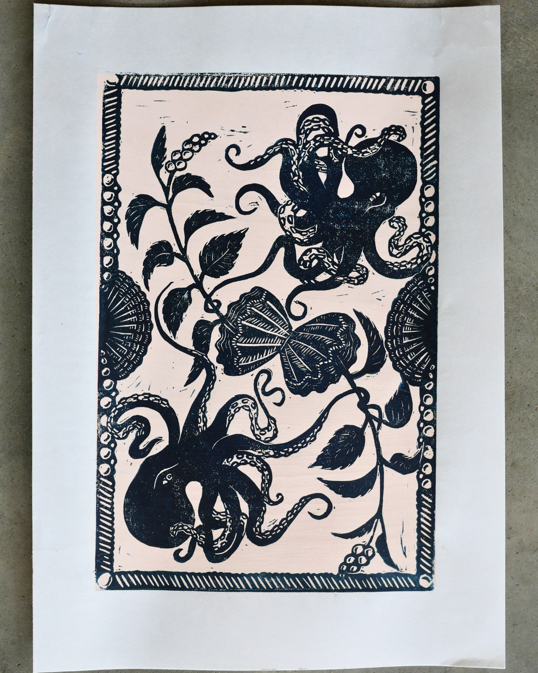 Black ink linocut print of octopuses and leaves on a beige background