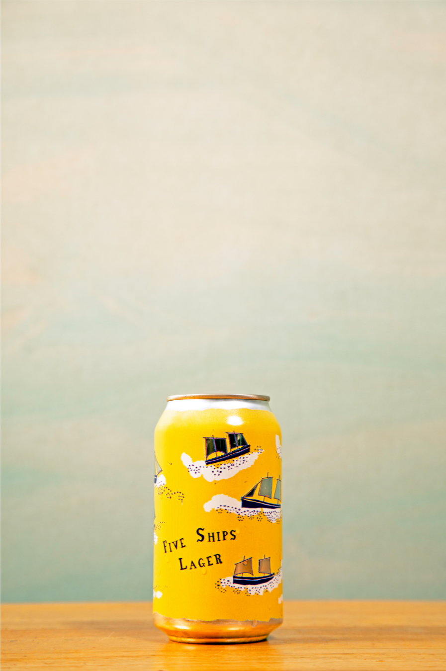 Yellow can of Five Ships Lager on a wooden surface with a gradient background