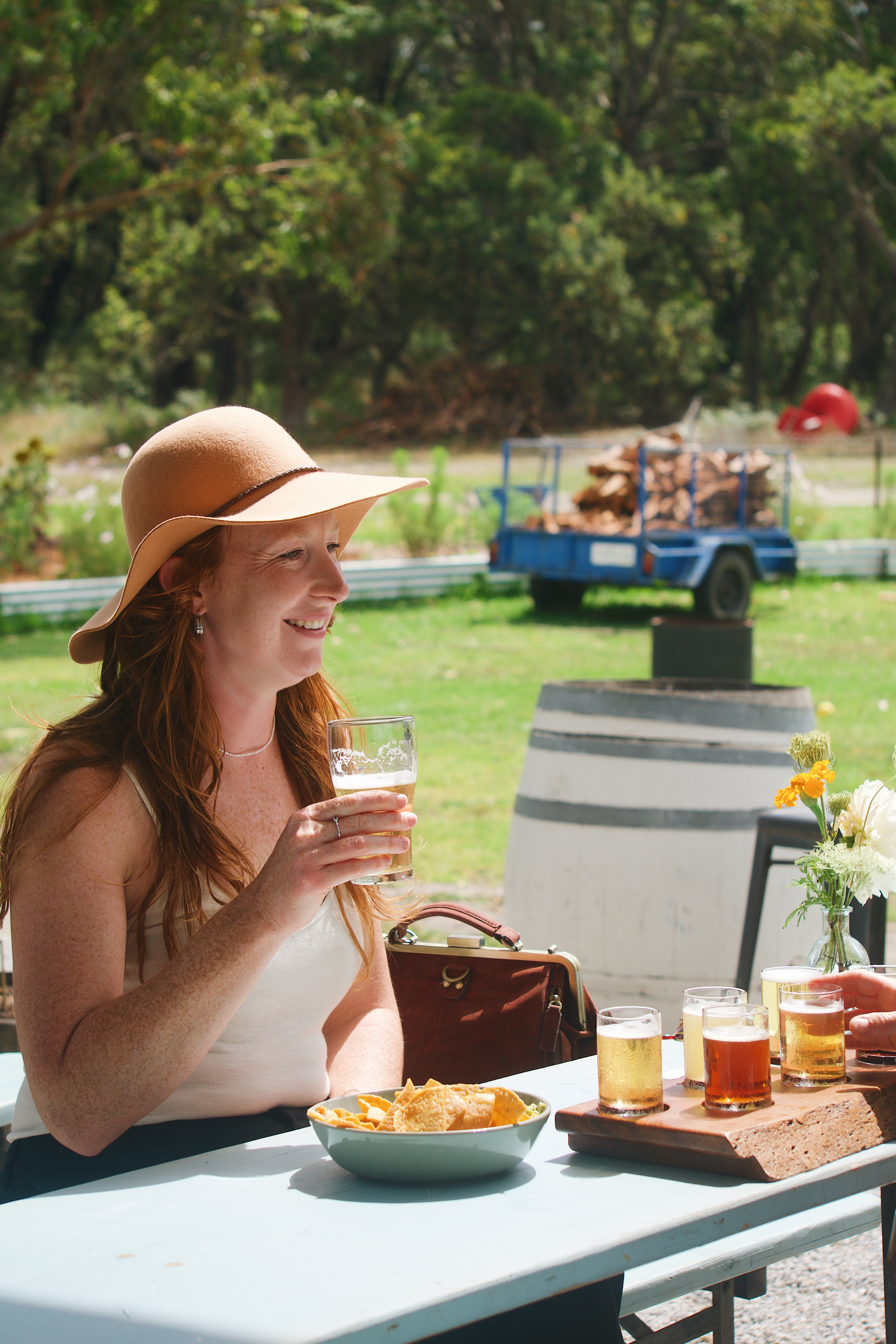 Woman sitting outdoors at a table with drinks and food, surrounded by greenery at aiors Grave Brewing Dunetown